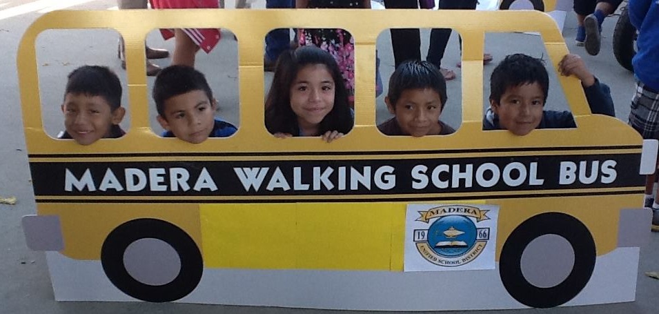 Children pose in the windows of a carboard cut-out walking school bus.