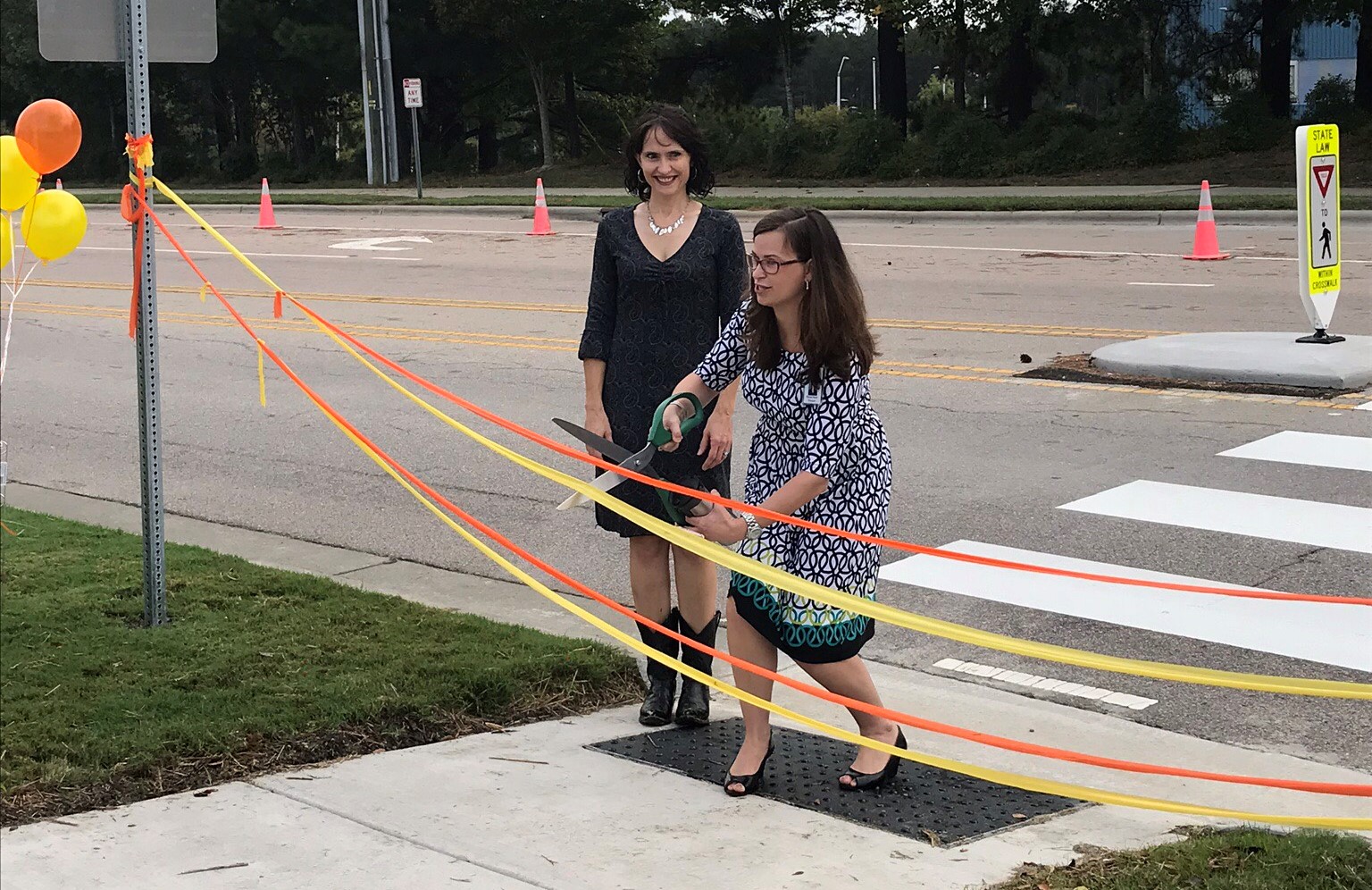 Two woman stand at a crosswalk.