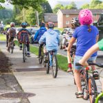 A line of students bike on a sidewalk.