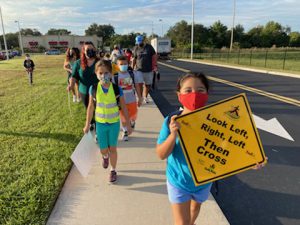 Child walking on a sidewalk holds a sign that reads: "look right, look left, then cross."