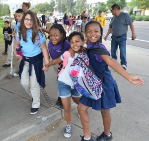 A group of children walk along a sidewalk. together