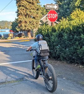 A child wearing a backpack riding an ebike at a stop sign.