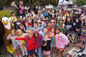 A large group of elementary students and adults with an eagle school mascot wave to the camera.