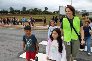 Students with an adult in a high visibility vest cross the street at a crosswalk.